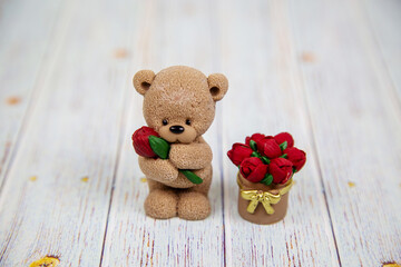 Sweets in the form of a gray bear with a flower and a basket of red roses on a gray wooden table. Confectionery drinks tea coffee.