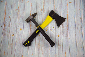 A carpenter's axe with a yellow handle and a hammer lying crosswise on a gray wooden table. Tools, construction, manufacturing, design, structures.