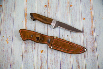 A hunting knife with a brown leather sheath on a gray wooden table. Tools, edged weapons, hobbies, hunting.