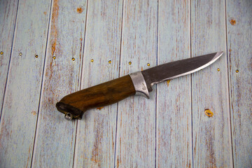 A hunting knife with a handle made of brown wood on a gray wooden table. Tools, edged weapons, hobbies, hunting.