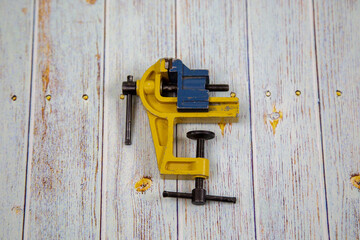 A small yellow vise on a gray wooden table. Tools, construction, manufacturing, design, structures.