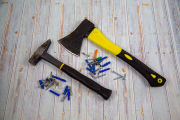 An axe, a hammer with dowels and screws on a gray wooden table. Tools, construction, manufacturing, design, structures.