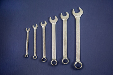 Metal wrenches arranged in a row on a blue background. Tools, construction, manufacturing, design, structures.