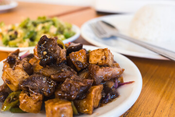 Stir-fried spicy tofu and pork, known locally as Tokwa Baboy, served with vegetables and rice at a Filipino restaurant.