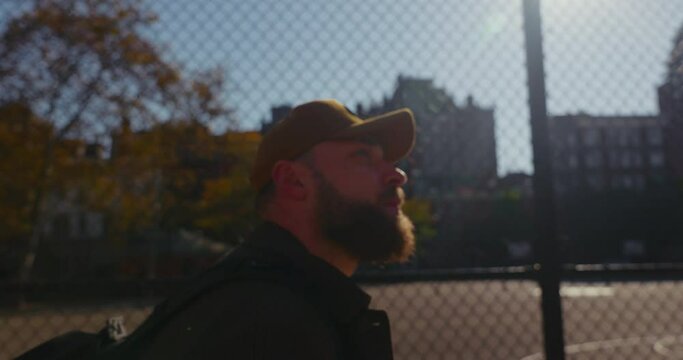 Close-up of handsome bearded male with a cap walking in sunny urban suburbs of New York.