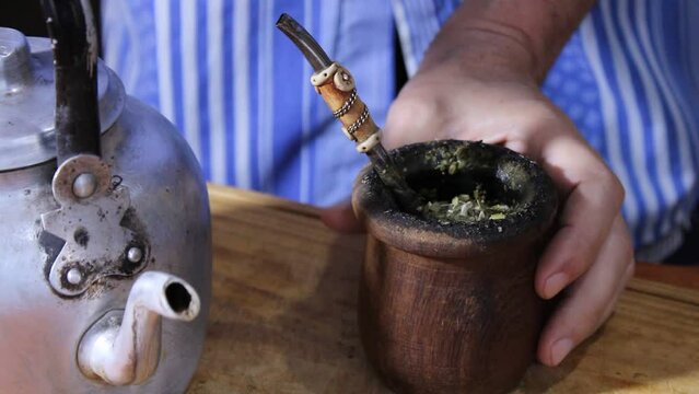 Tradiciones Argentinas de la yerba mate. El hombre coloca el chorrito de agua caliente con la vieja pava o tetera de aluminio en el mate de calabaza sobre la mesa de madera, formando un original video