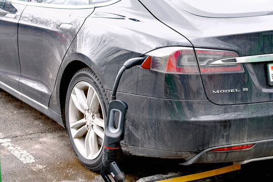 Minsk, Belarus. Feb 4, 2024.  Tesla Model S pluged to charge point at parking lot, electric car charging in cold winter season. Charging EV car, rear view.