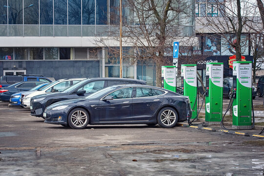 Minsk, Belarus. Feb 4, 2024.  Tesla Model S parked at snowy parking lot and charge battery at electric charge point, electric car charging in cold winter season. Charging EV car