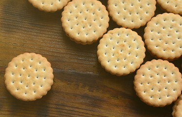 A round sandwich cookie with coconut filling lies in large quantities on a brown wooden surface. Photo of edible treats on a wooden background with copy space