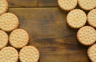 A round sandwich cookie with coconut filling lies in large quantities on a brown wooden surface. Photo of edible treats on a wooden background with copy space