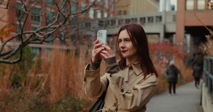 Attractive brunette female taking pictures filming video using smartphone in autumnal High Line Park in New York