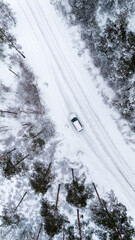Top down view of white car on snowy road in winter forest