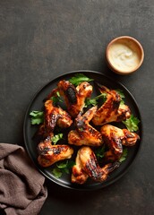 Bbq chicken wings served with sauce over dark stone background