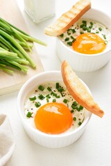 Baked eggs (Eggs en cocotte) with cream, сheese and green onion in ramekins