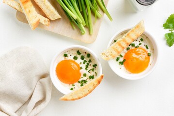 Eggs en cocotte (baked eggs) with cream, сheese and green onion in ramekins