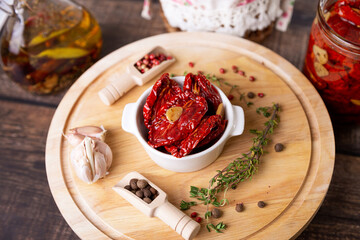 Sun-dried tomatoes in olive oil in a white bowl with pepper, garlic and thyme on a wooden board. Home cooking, rustic style. Selective focus, close-up.