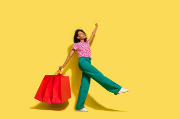 Full size photo of pretty positive girl hold store shop bags empty space isolated on yellow color background