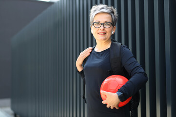 A fit Caucasian woman takes a break from outdoor fitness, holding a water bottle with a smile.