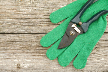 There are scissors with green handles and green work gloves on a white wooden table. Garden hand pruners. Garden shears. Sharp trimmers for pruning trees and shrubs.Copyspace
