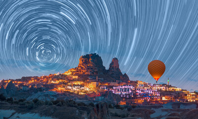 Hot air balloon flying over Goreme village with star trail at twilight blue hour - Cappadocia,...