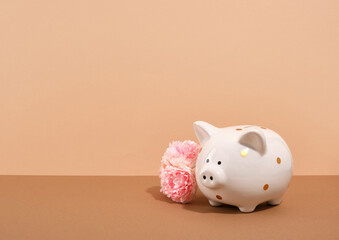 Piggy bank and pink flowers on a beige background. Copy space for text. Piggy bank savings concept.