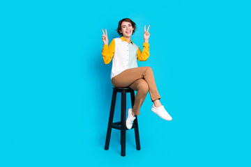 Photo of positive cheerful girl manager sit stool make v sign isolated blue color background