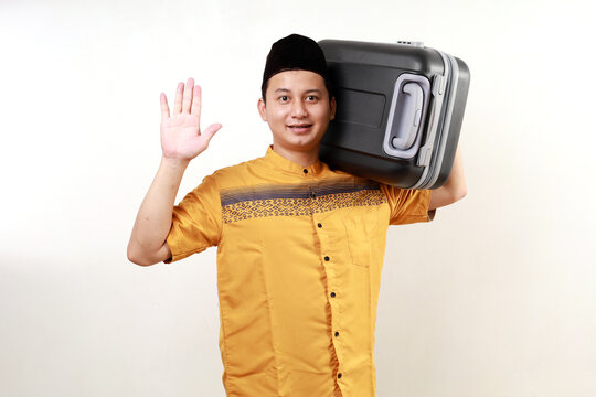 Happy asian muslim man carrying travel suitcase. Going mudik or travel to hometown for Ramadan eid mubarak celebration