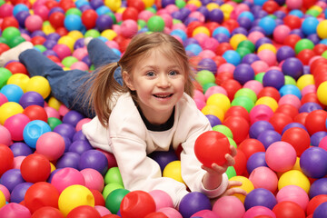 Happy little girl lying on colorful balls in ball pit