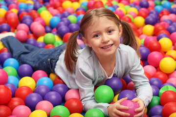 Fototapeta na wymiar Happy little girl lying on many colorful balls in ball pit