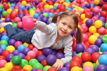 Happy little girl lying on many colorful balls in ball pit