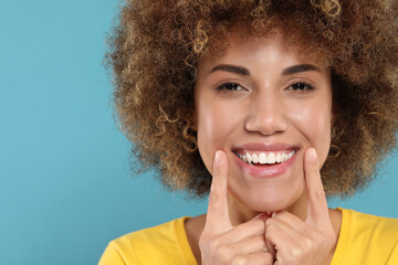 Fototapeta na wymiar Woman showing her clean teeth and smiling on light blue background, space for text