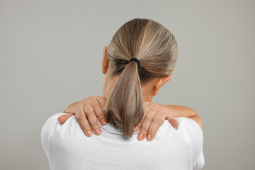 Mature woman suffering from pain in her neck on grey background, back view