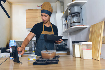 young man at home touching phone screen paused video tutorial he is watching while preparing cake