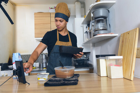 young man at home touching phone screen paused video tutorial he is watching while preparing cake