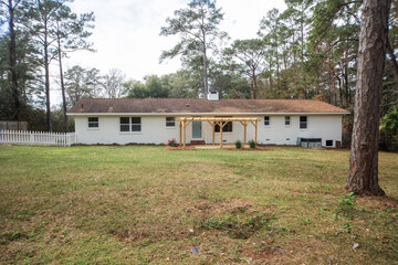 The rear back exterior of a newly painted and renovated white brick ranch style house with a large...