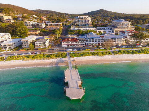 Aerial view of a coastal township behind an unusually shaped jetty and sandy beach