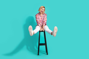 Full length photo of nice young lady sit chair stretching legs dressed stylish pink print garment isolated on aquamarine color background