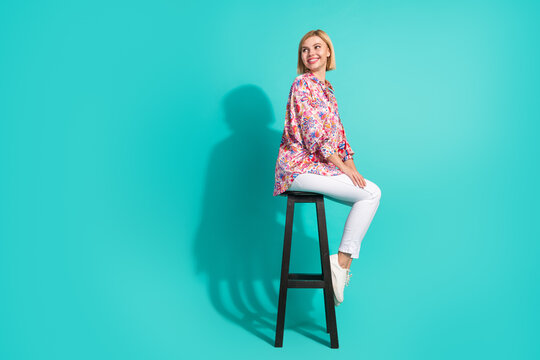Full size photo of young woman sit chair turn around look empty space dressed stylish pink clothes isolated on aquamarine color background