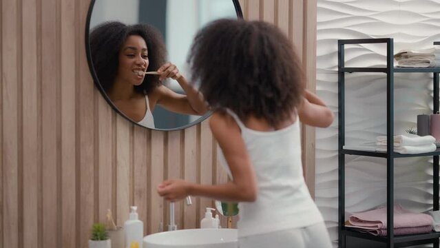 African American woman using tooth paste toothbrush brushing white teeth looking in mirror girl female with whitening toothpaste enjoy mouth oral dental hygiene procedure morning gums care routine