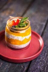 Chia Seed Pudding with Mango and Berries in Glass Jar on Red Plate