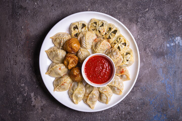 Uzbek samsas and manti with meat, pumpkin and greens on a plate with red sauce