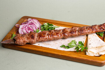 Delicious and juicy chicken shish kebab on a wooden board with onion rings and parsley.