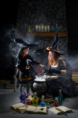 Halloween magic. Young girls in witch costumes with a cauldron, a book of spells and a potion in a...