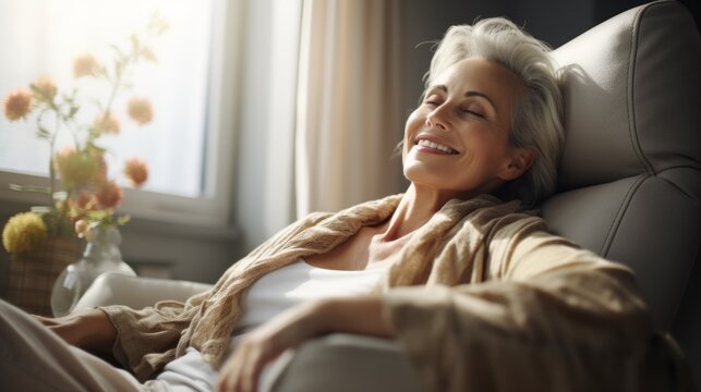 A relaxed elderly woman is sitting in a comfortable chair and enjoying the sunlight coming in from the window