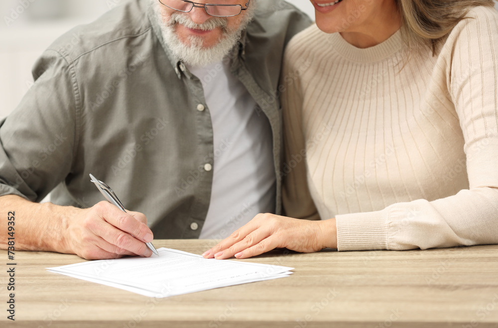 Sticker Senior couple signing Last Will and Testament at wooden table indoors, closeup