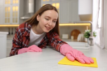 Woman cleaning white marble table with microfiber cloth in kitchen, selective focus