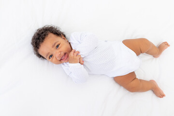 smiling African-American little baby on white bed in bedroom laughing