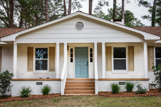 The front exterior entrance of a newly painted white siding brick ranch style house with a large yard that has been recently renovated