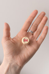 Lotto barrel with the number 84 in a woman's hand. Female hand. Lotto keg. A two-digit number. Woman 40 years old. Symbol of the 40th anniversary. Year of birth 1984. Hold in hand. Age metaphor.