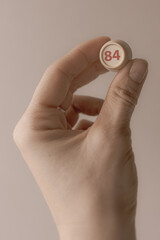 Lotto barrel with the number 84 in a woman's hand. Female hand. Lotto keg. A two-digit number. Woman 40 years old. Symbol of the 40th anniversary. Year of birth 1984. Hold in hand. Age metaphor.